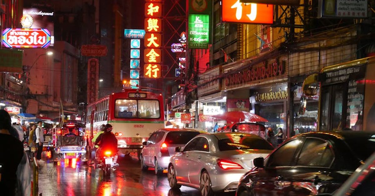 A lively night scene in Bangkok's Chinatown with busy traffic and illuminated neon signs.