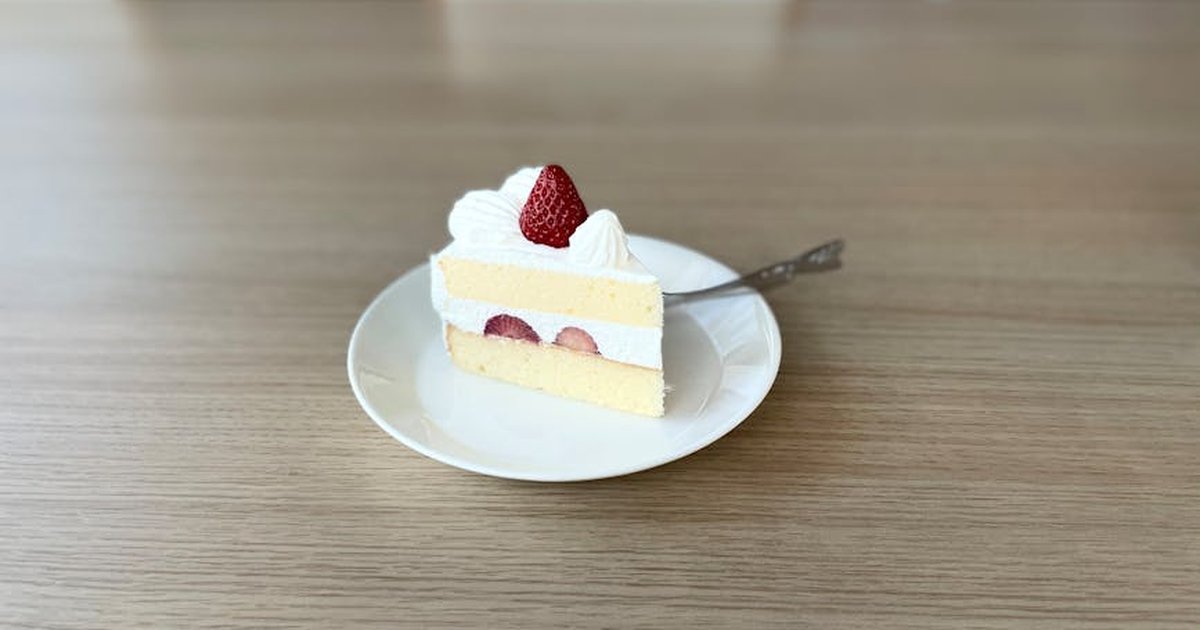 Sliced strawberry shortcake with whipped cream on a white plate, photographed indoors.