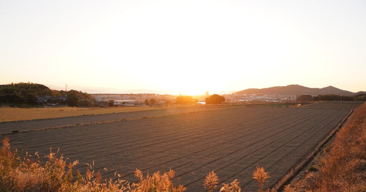 Tranquil sunset over freshly plowed fields with distant hills in the background.