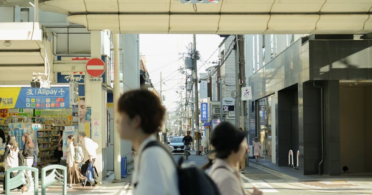 Busy street scene in Japan with pedestrians, shops, and traffic under daylight.