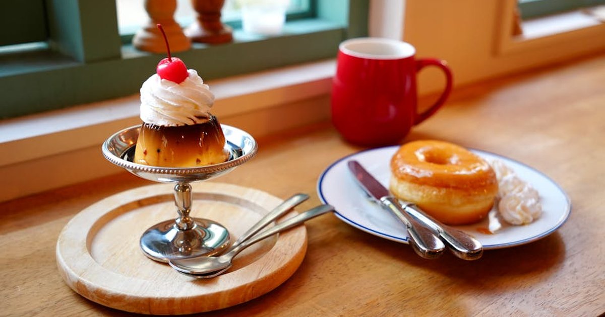 Delicious pudding and glazed doughnut on a wooden table with coffee in a cozy café setting.