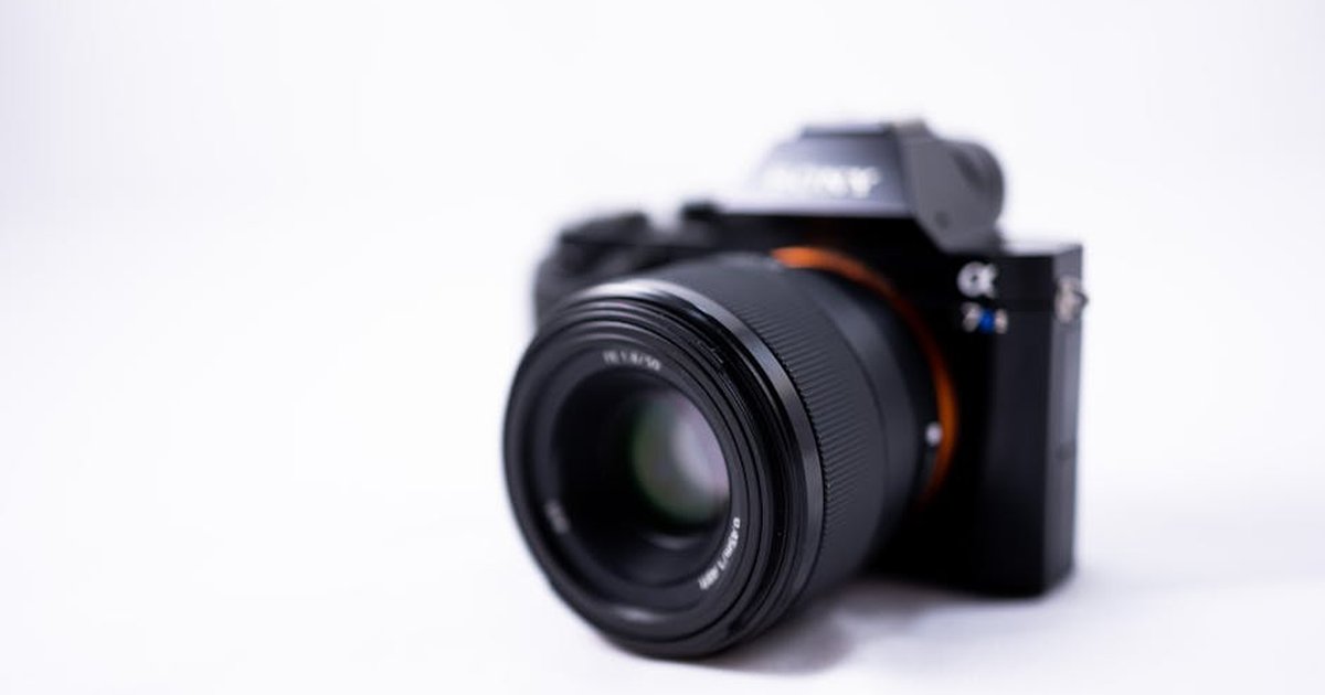 Closeup of contemporary digital black photo and video camera with lens placed against white blurred background