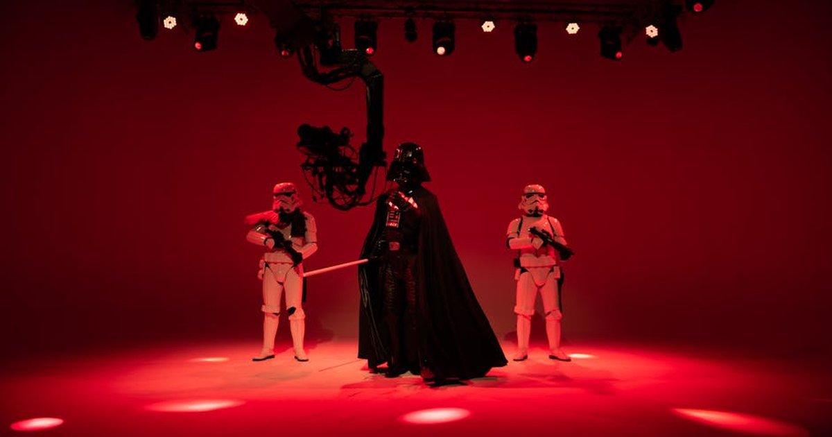 Three sci-fi characters in costumes pose under red studio lights, creating a dramatic scene.