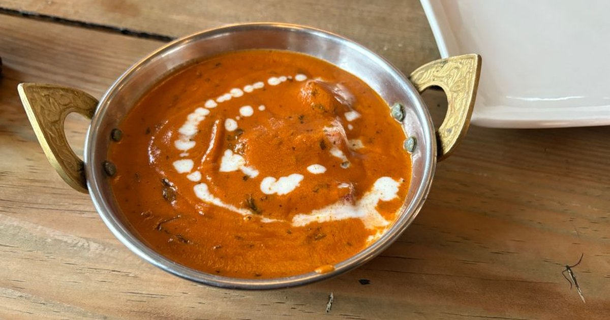 Authentic Indian butter chicken served in a brass bowl with creamy sauce, on a wooden table.