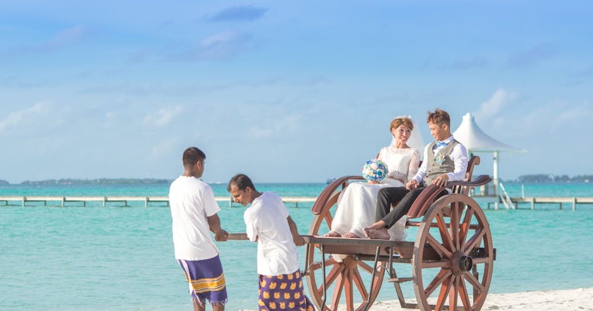 A joyful couple enjoys a cart ride on a scenic tropical beach, perfect for romantic getaway visuals.