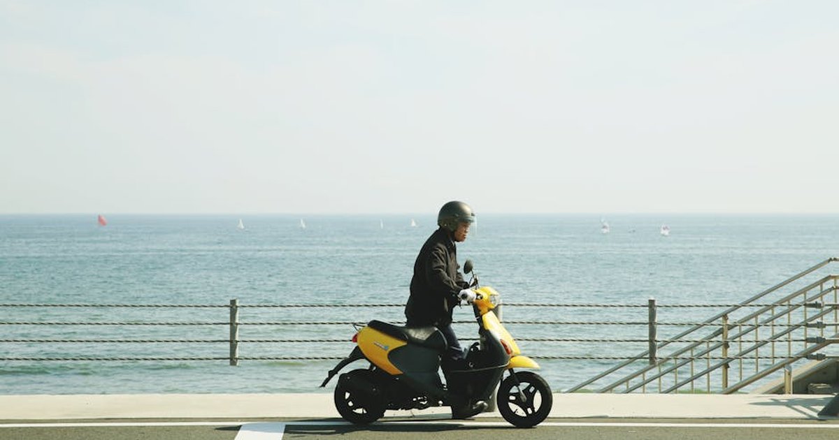 A man on a yellow scooter rides by the ocean in Fujisawa, Japan.