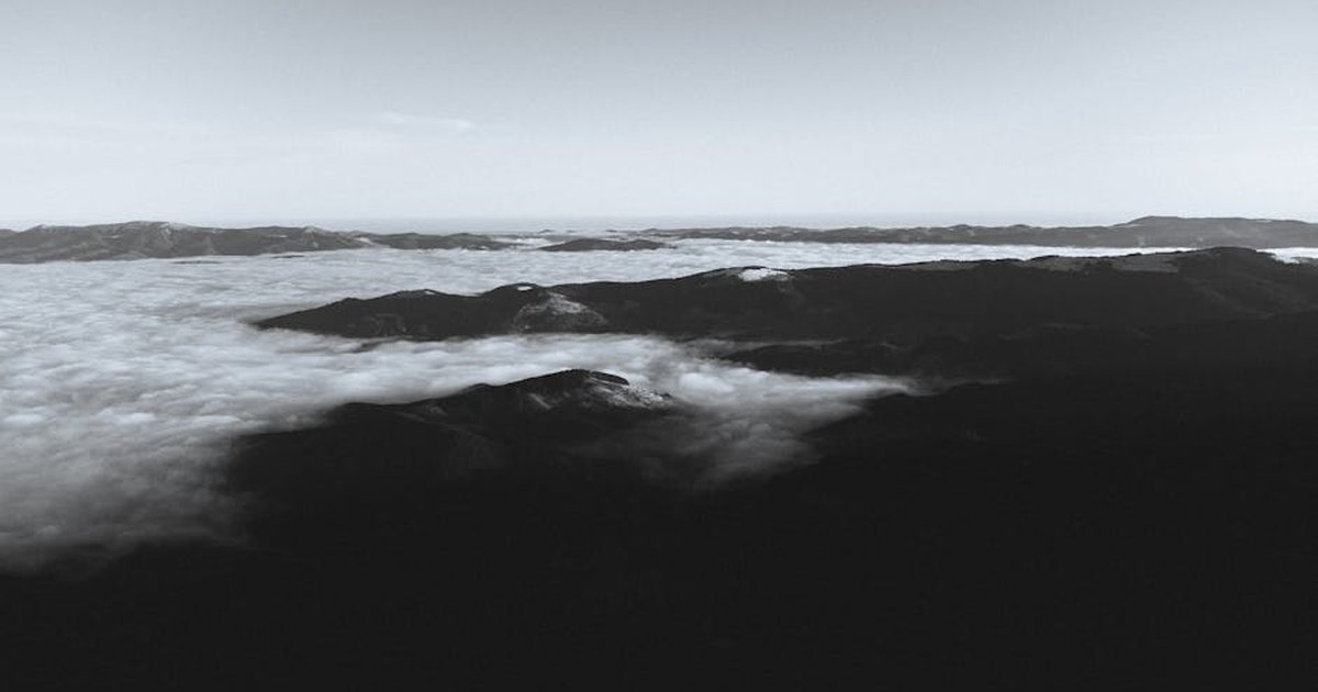 A stunning black-and-white aerial shot of mountains covered in clouds, showcasing the beauty of Romania's landscapes.