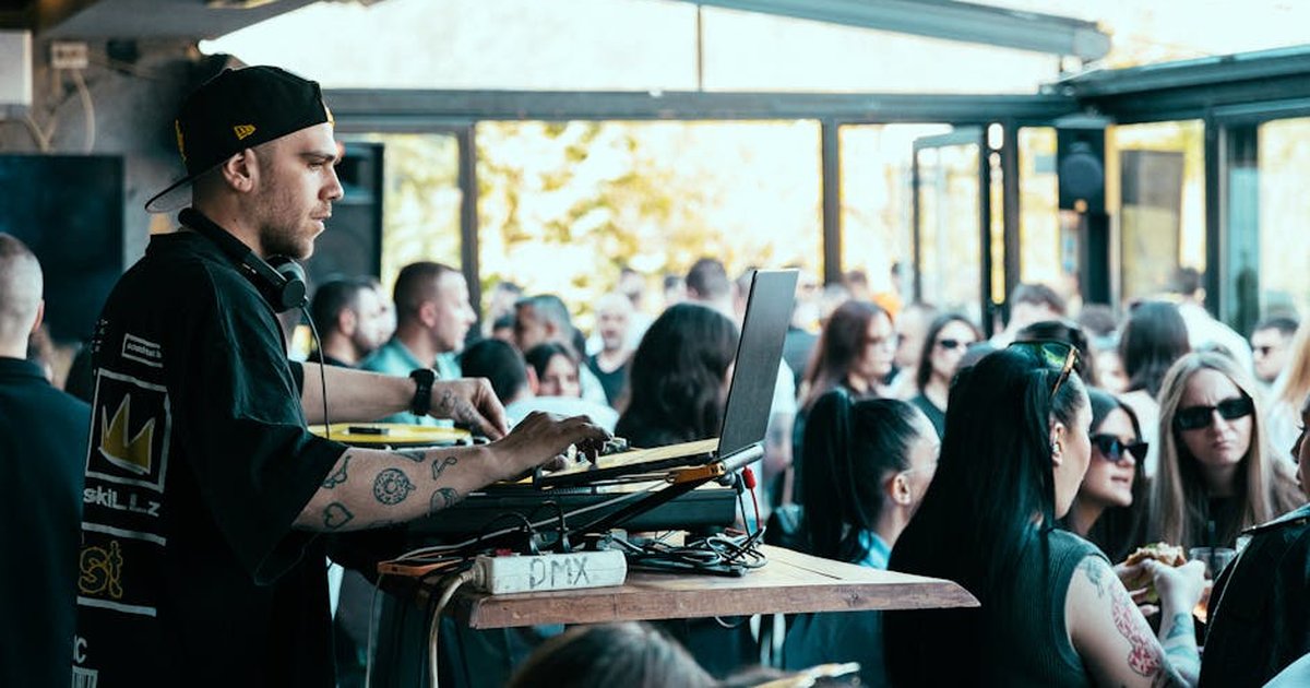 A DJ mixes music on a laptop at a vibrant indoor party with an energetic crowd.