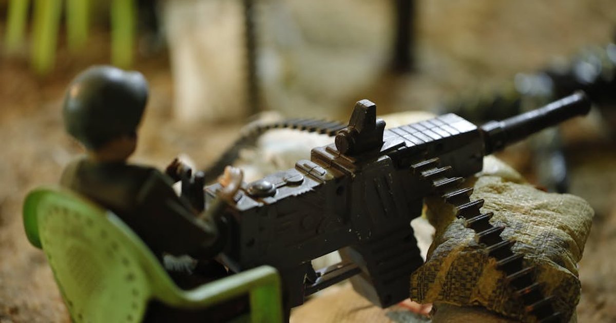 Close-up of a toy soldier in a diorama setting, holding a plastic machine gun and seated in a green chair.