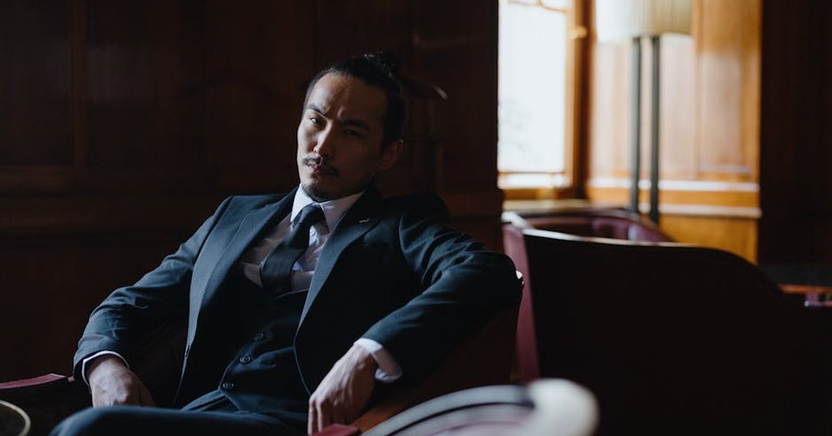 Man in formal business attire sitting in a stylish, dimly lit room.