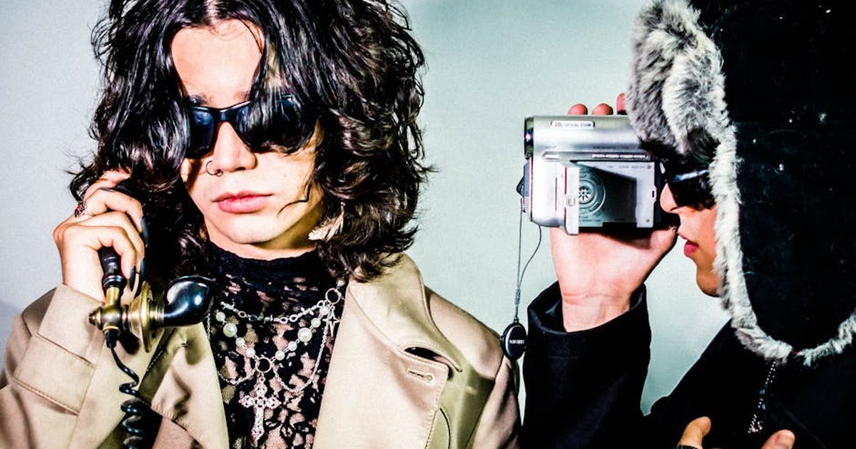 Two stylish adults posing with a vintage phone and camcorder in a retro, artistic setting.