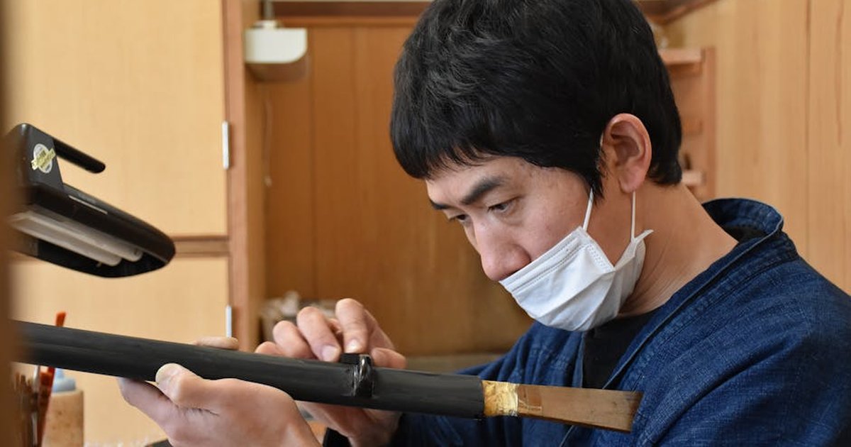 Focused Japanese craftsman working on samurai sword indoors, showcasing traditional craftsmanship.