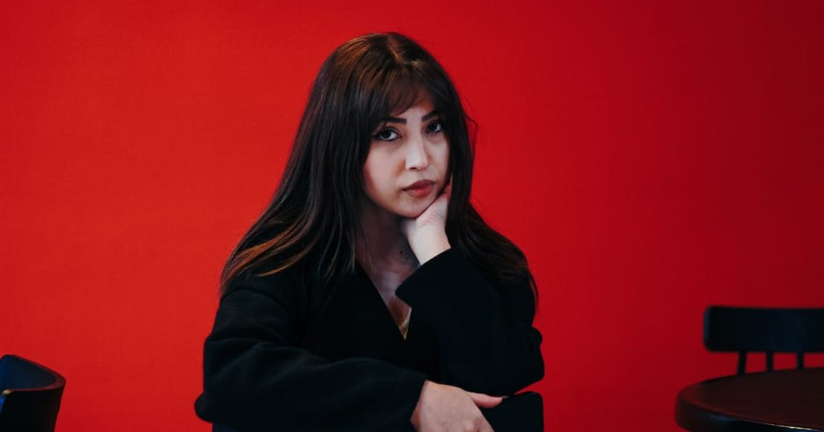 Stylish portrait of a young woman in a Tehran cafe, set against a bold red background.