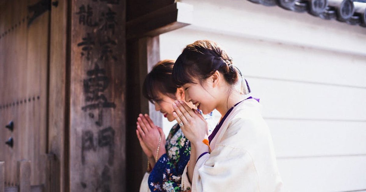 Two women in kimonos praying at a Kyoto temple gate, embracing Japanese tradition.