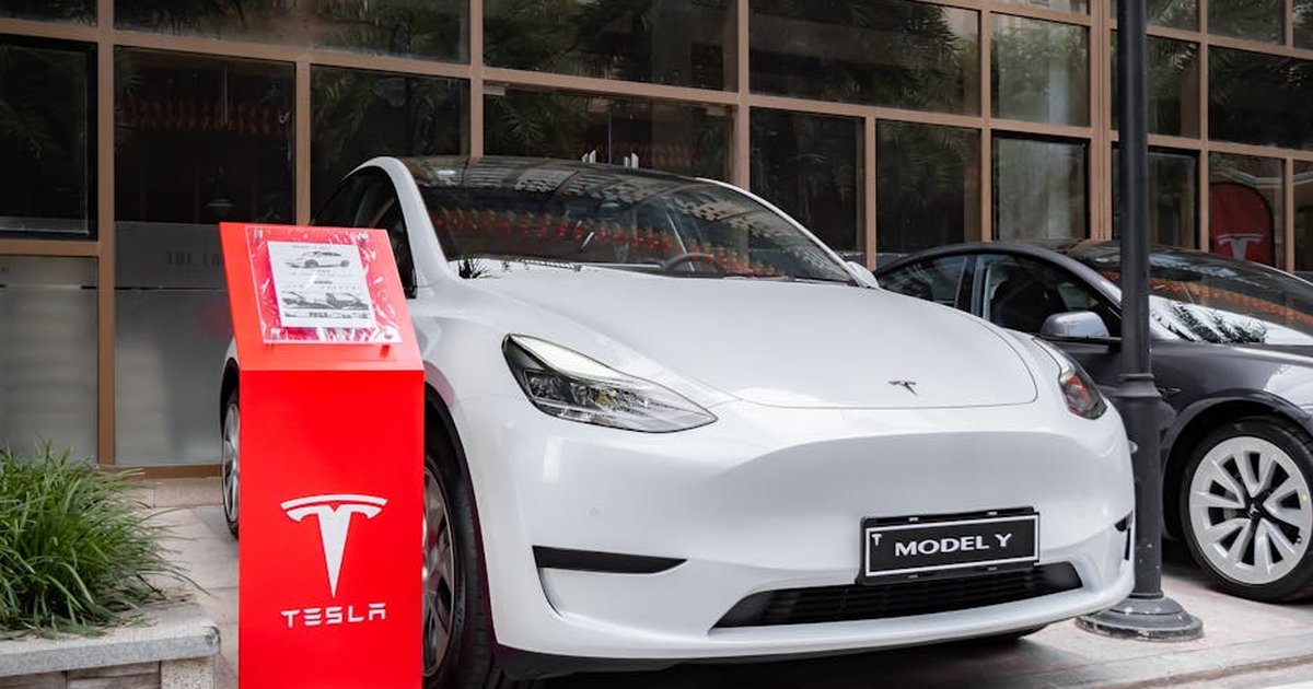 Tesla Model Y parked outdoors with a red display stand in front. Modern and sleek automotive design.