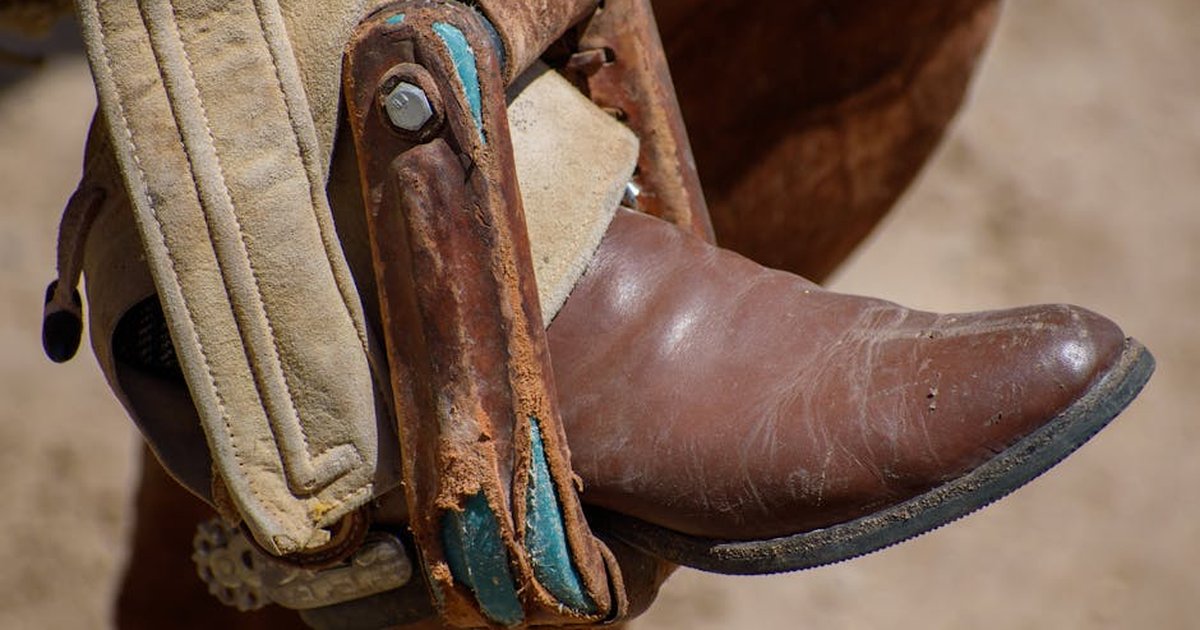 Close-up of a traditional Mexican cowboy boot in a stirrup during an outdoor charrería event.