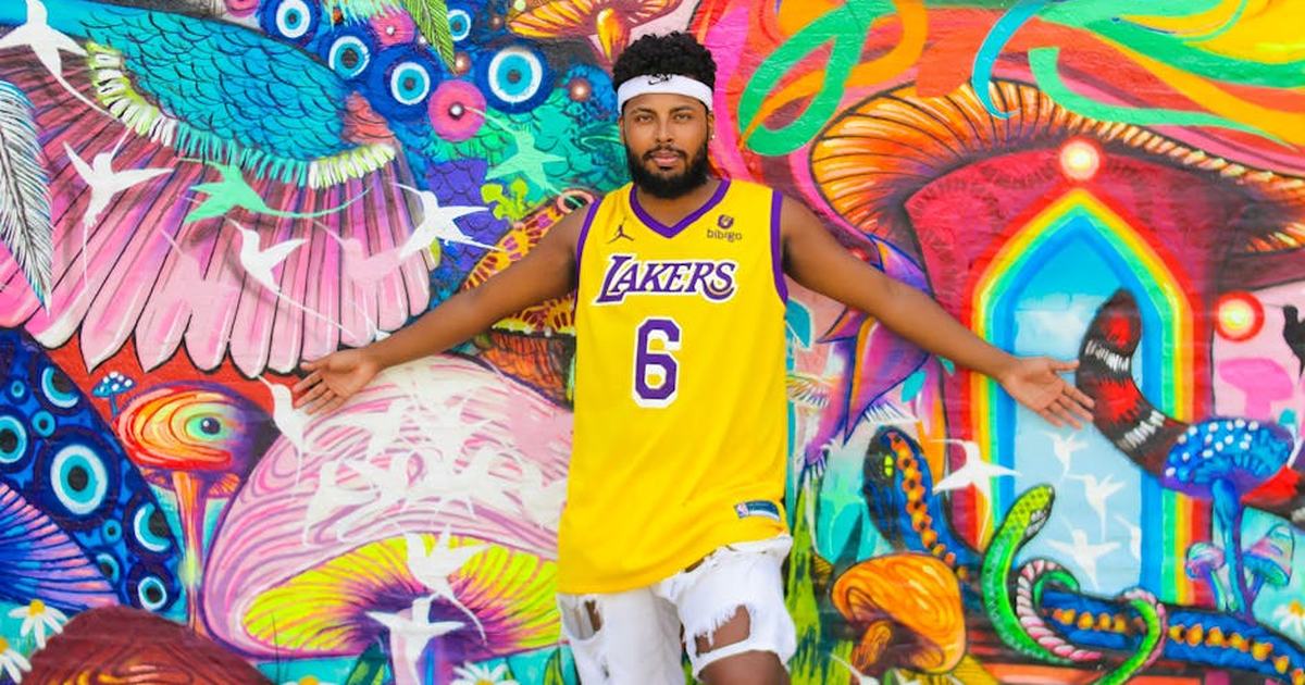 Man in Lakers jersey posing against a colorful mural wall, showcasing vibrant art and style.