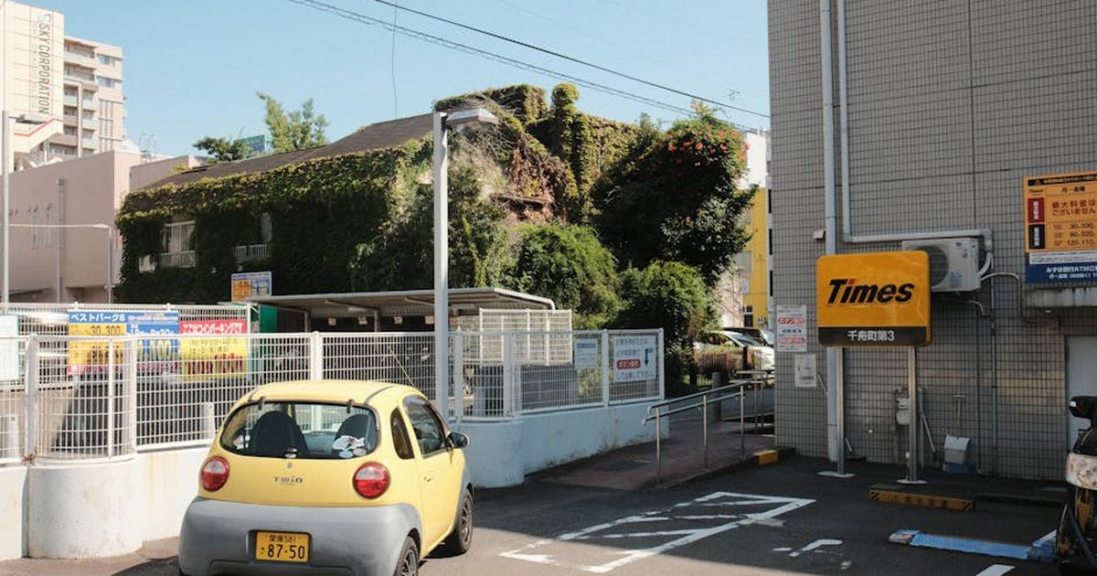 Yellow car in an urban Japan parking lot with ivy-covered building.