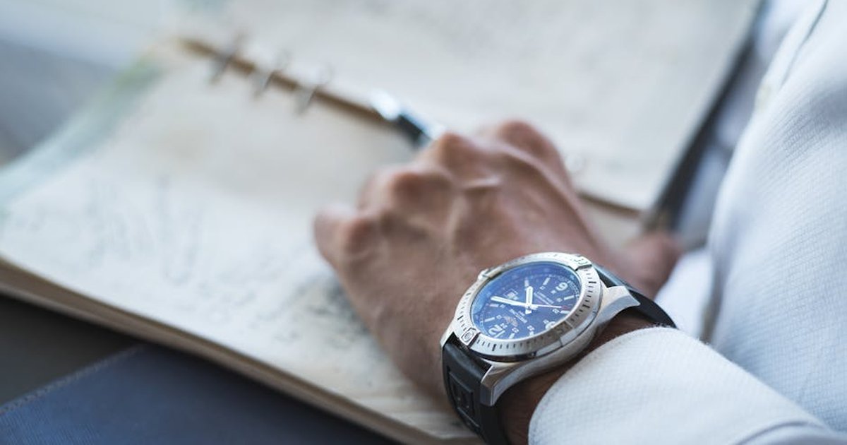 Detailed shot of a wristwatch and an open leather-bound notebook, showing a handwritten page.