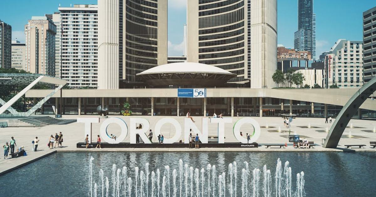 View of Toronto City Hall with vibrant fountains and iconic city sign under a blue sky.