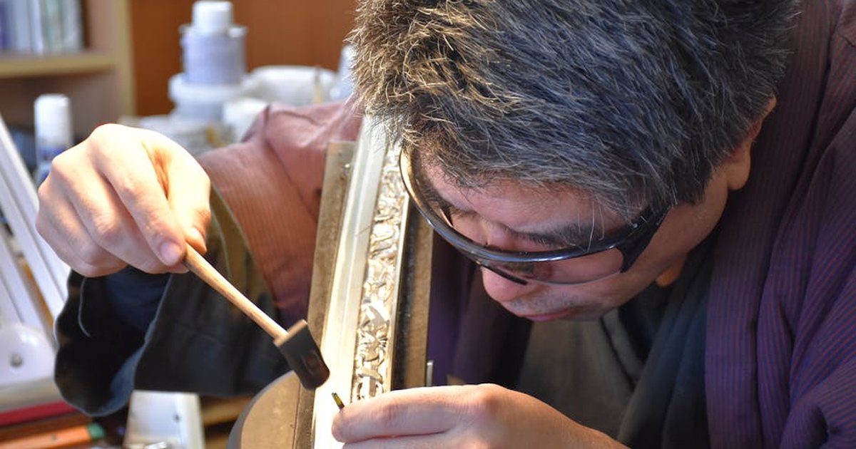 A skilled Japanese craftsman intensely engraving a metal piece in his workshop, showcasing traditional artistry.