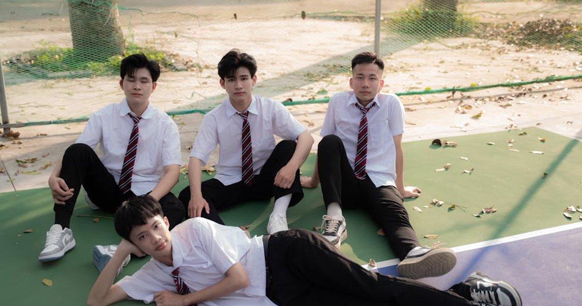 Four teenage boys in uniforms relaxing on a sunny basketball court.