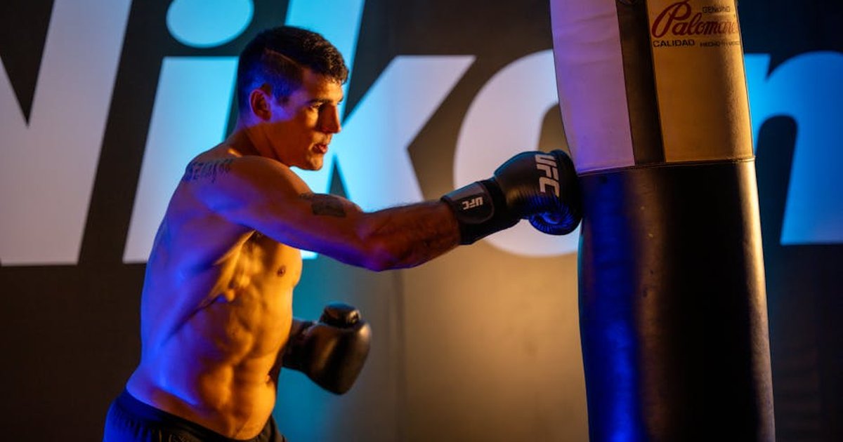 A male boxer trains intensely with a punching bag indoors at a gym in Mexico City.