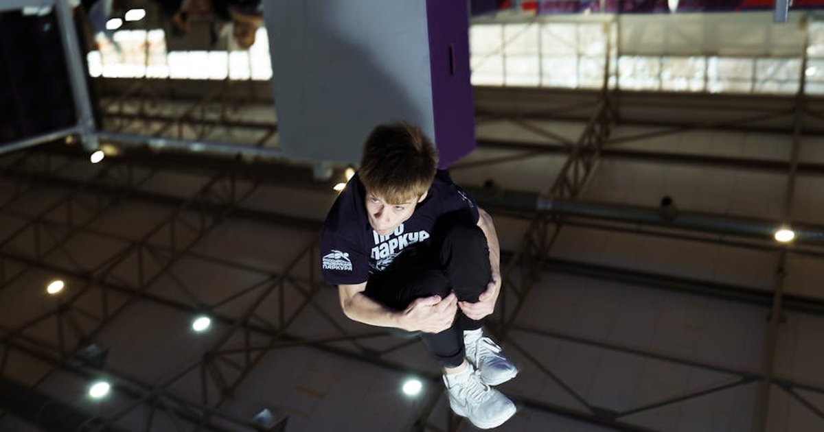 A young man performs a parkour flip indoors, showcasing athletic skills and agility.
