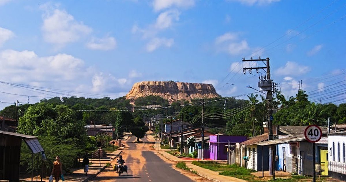 A vibrant town road with power lines leads to a majestic mountain under a blue sky.