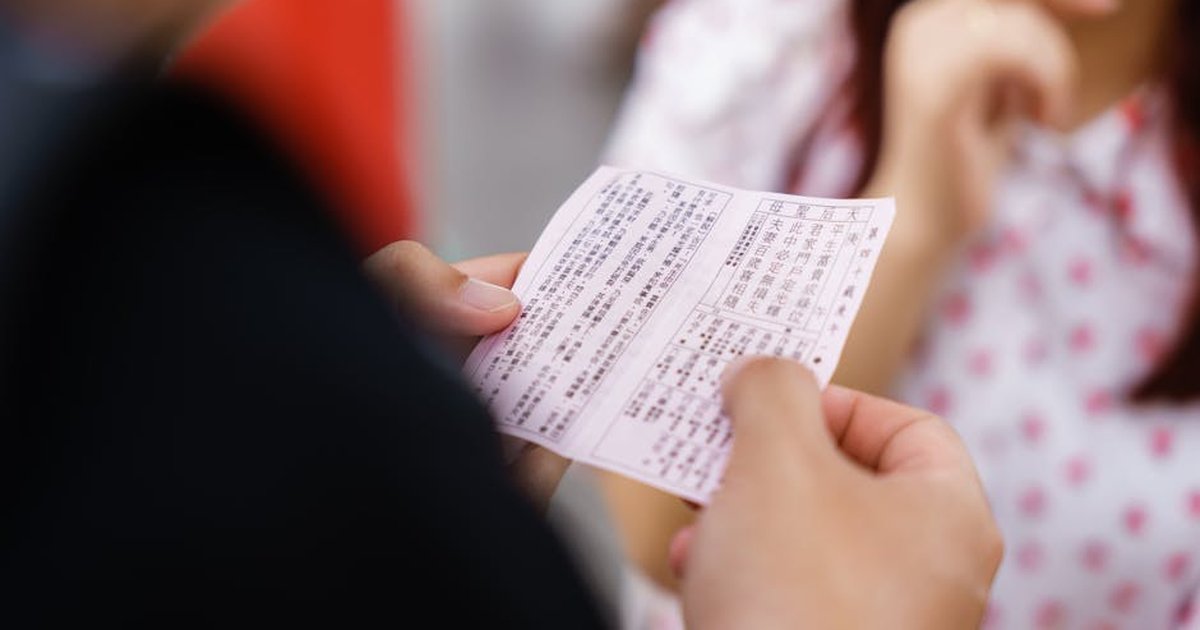 Two people interacting indoors, holding a document with Asian characters, focus on hands.