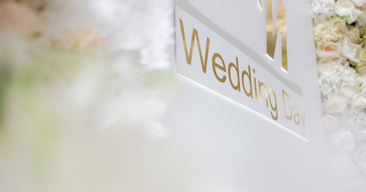 Luxurious wedding day sign with white and gold details surrounded by soft focus flowers.