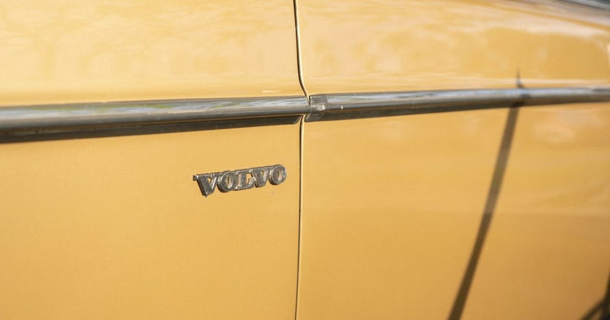 Close-up of a vintage Volvo emblem on a mustard yellow classic car door, emphasizing retro automotive style.
