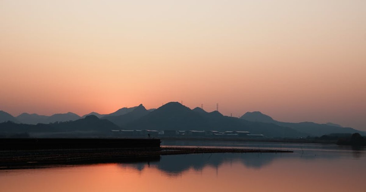 Beautiful sunset view over a calm lake with mountains silhouetted in the background, reflecting serene colors.