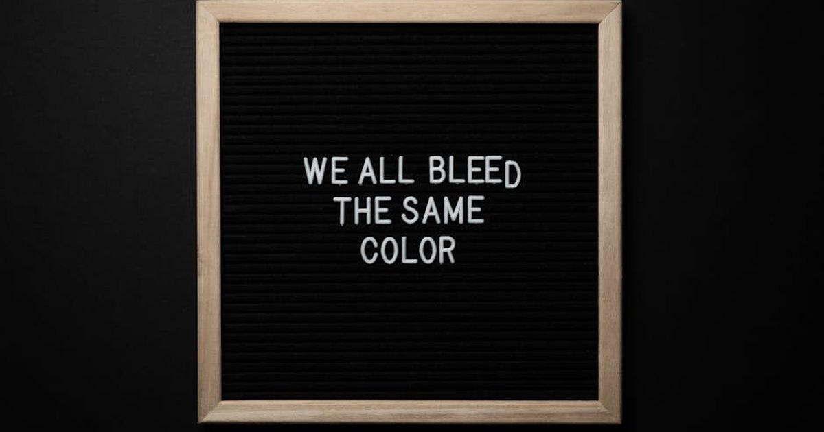 Top view of black signboard with phrase We All Bleed Same Color on surface on black background