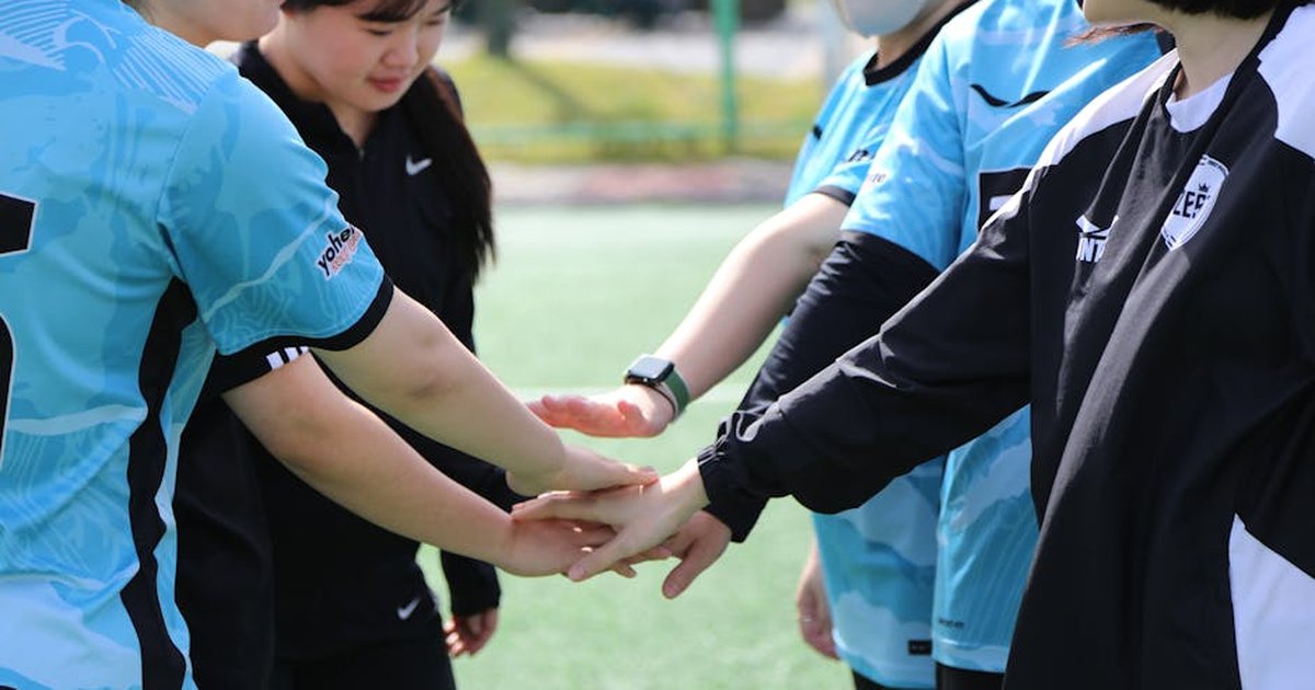 Women football players unite in a triumphant team gesture outdoors.