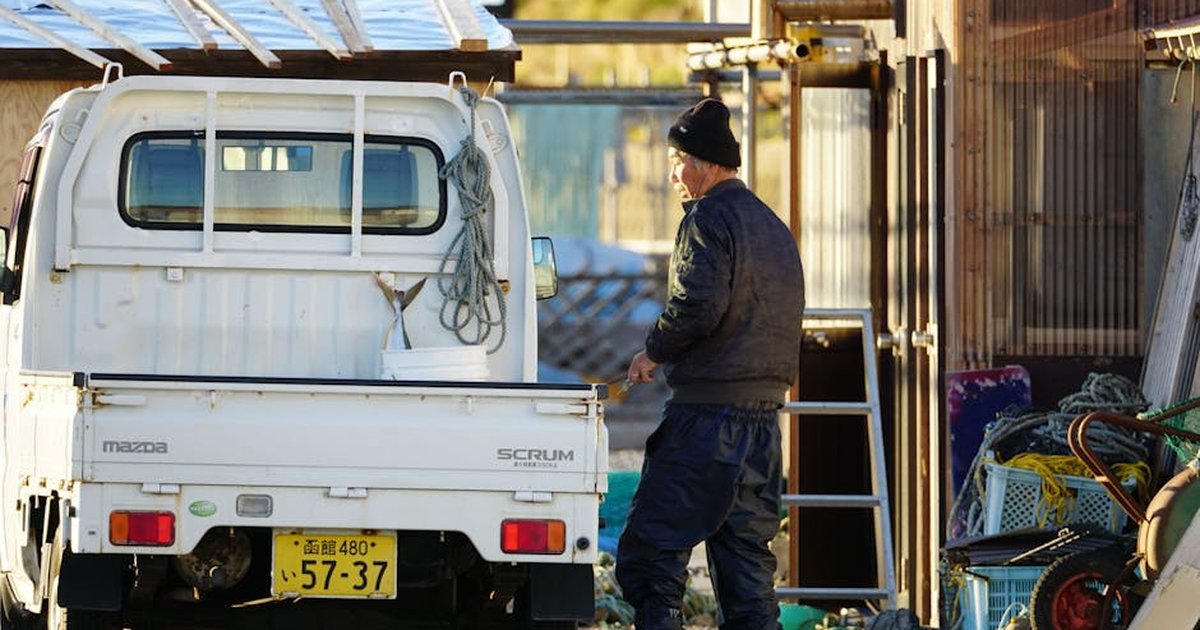 Elderly fisherman working by his truck with ropes and crates outdoors in Japan.