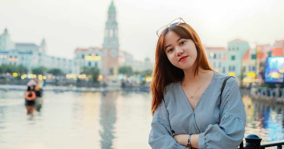 Young woman with long hair posing by a scenic urban waterfront.