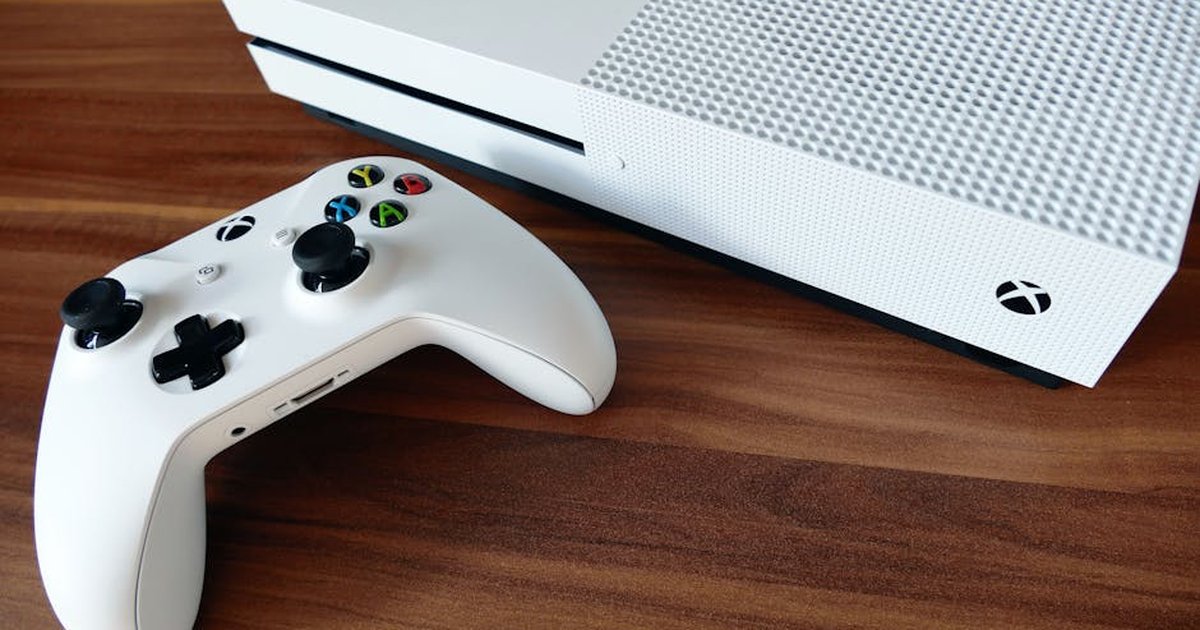 Close-up of a white Xbox console and controller on a wooden surface, ideal for gaming enthusiasts.