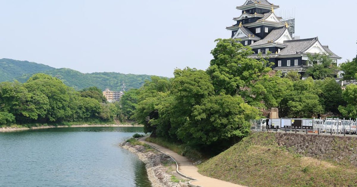 Stunning view of Okayama Castle by the river surrounded by lush greenery in Japan.