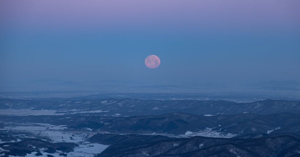 Stunning winter mountain landscape in China with a full moon rising in the twilight sky.