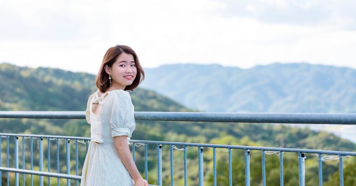 A smiling woman in a white dress on an outdoor balcony with scenic mountain views.