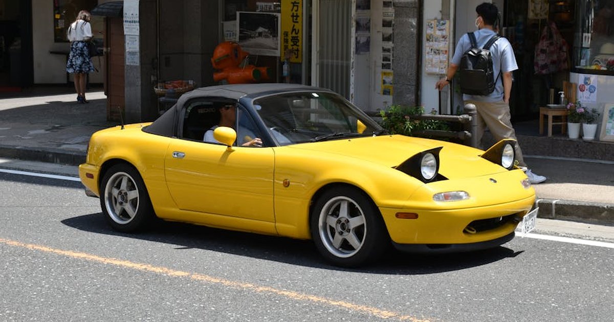 A vibrant yellow sports car driving through a bustling city street on a sunny day.