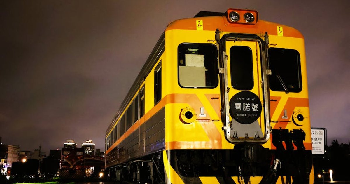A vibrant yellow and orange train captured under city lights in Kaohsiung, Taiwan.