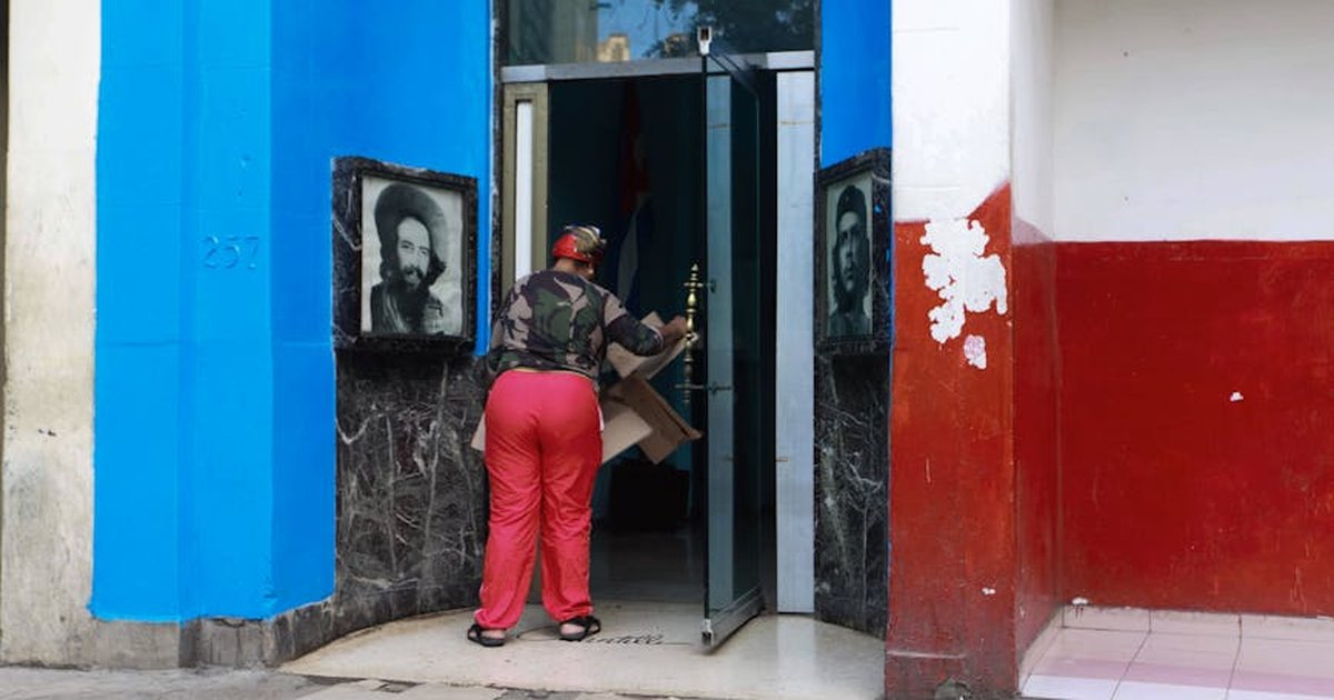 A person carrying cardboard boxes enters a blue and red building with portraits on the walls.