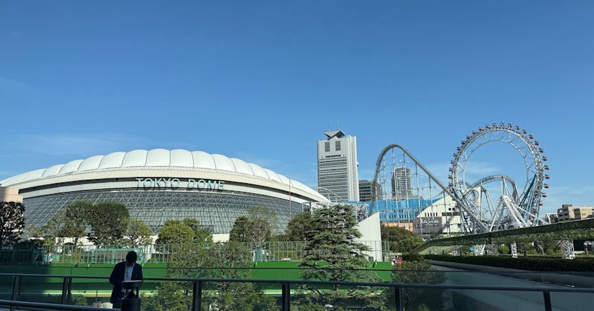 A clear day view of Tokyo Dome with amusement rides and skyline in the background.