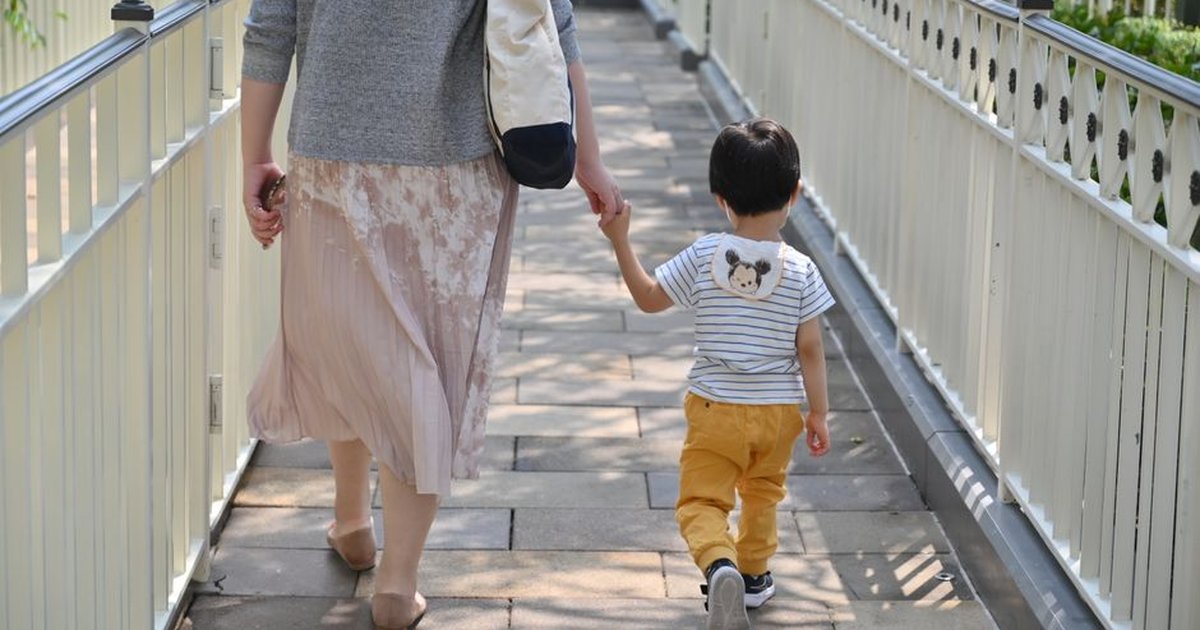 A mother and son holding hands walking on a sunlit cobblestone path.