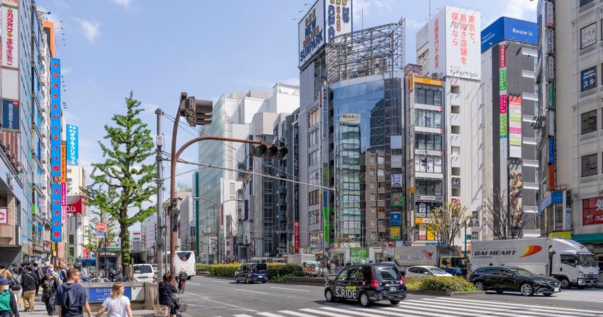 Lively urban street scene in Shinjuku, Tokyo featuring pedestrians, vehicles, and modern architecture.