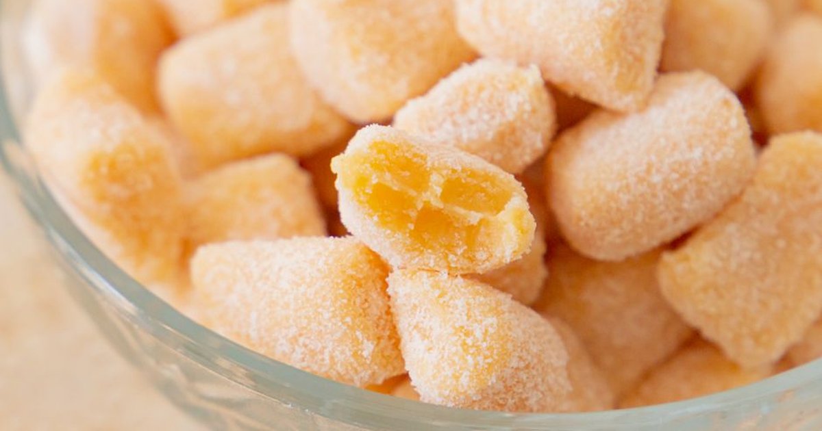 Close-up of sugar-coated passion fruit candies in a glass bowl, showcasing vibrant yellow hue.