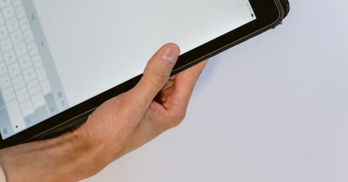A close-up image of a hand holding a black tablet showing an open keyboard on the screen.