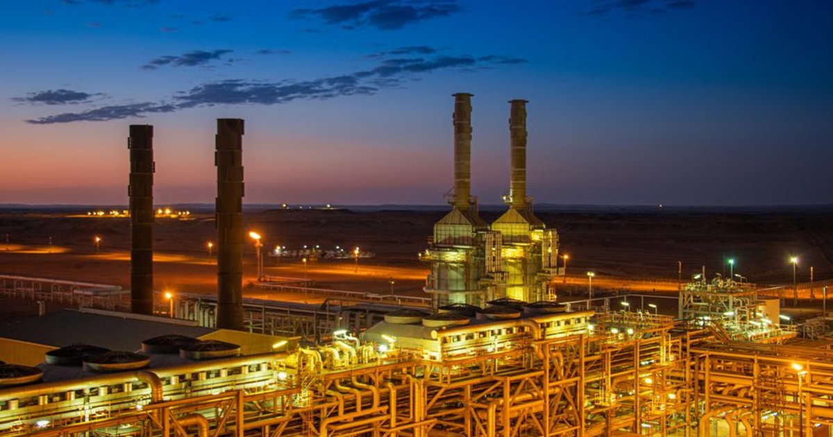 Aerial view of an illuminated factory with chimneys at sunset, showcasing industrial architecture.